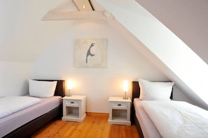 A bedroom with two beds, wooden flooring, and a ceiling with a sloped design. - Holiday apartment in Sylt with 2 bedrooms (Keitum)