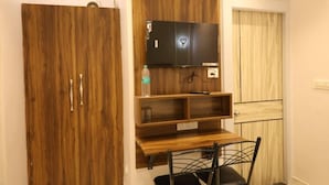 A room with a wooden wardrobe, a mounted television, and a small wooden table.