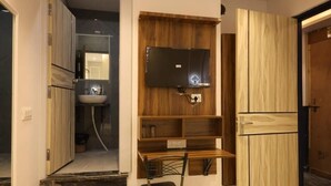 A room with a wooden vanity, a mirror, a black chair, and a television mounted on the wall.
