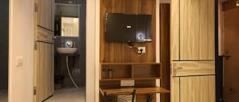 A room with a wooden vanity, a mirror, a black chair, and a television mounted on the wall.