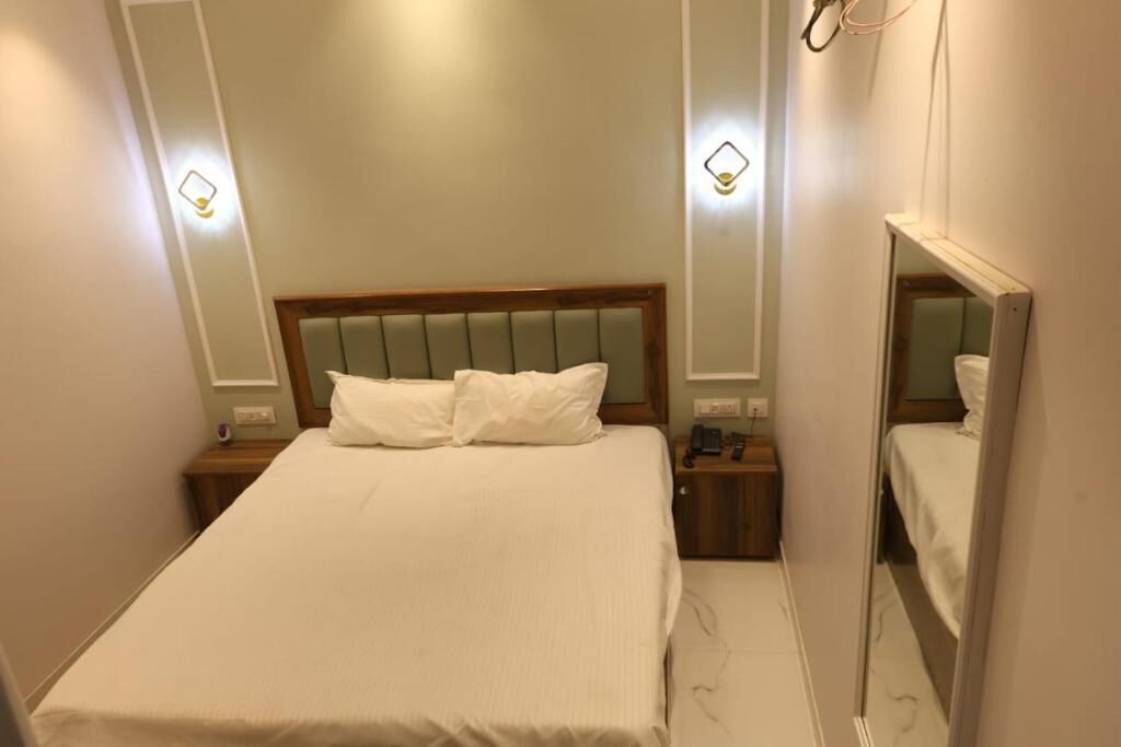 Una habitación de hotel con una cama, mesitas de noche, un espejo y luces en la pared.