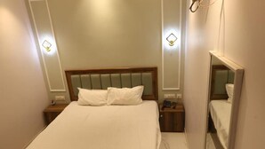 Habitació d'hotel amb un llit, taules de nit, un mirall i llums penjades a la paret.