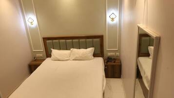 Una habitación de hotel con una cama, mesitas de noche, un espejo y luces en la pared.