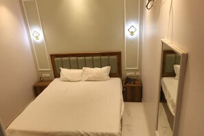 A hotel room with a bed, bedside tables, a mirror, and wall-mounted lights. - HOTEL SHREE KARNI PALACE (Bulandshahr)