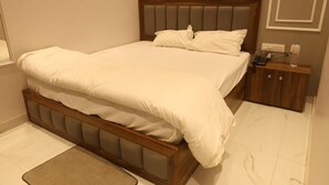 Un llit ben fet amb un capçal de fusta i una petita taula de nit amb un telèfon i una ampolla.