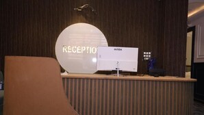 Una taulell de recepció amb un rètol que diu 'RECEPTION' i un monitor d'ordinador amb l'etiqueta 'INTEX'.