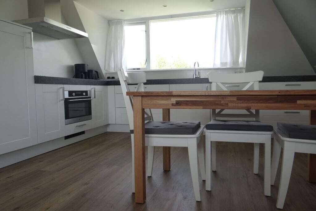 A modern kitchen with white cabinetry, a built-in oven, and a dining area with a wooden table and white chairs.