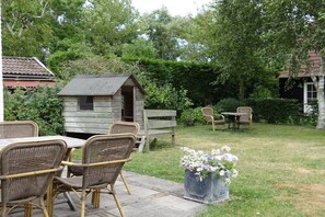 A patio with wicker furniture, a small wooden playhouse, and a planter with flowers. - Apartment in Oostkapelle with swimming pool (oostkapelle)