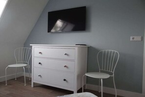 A room with a white dresser, two white chairs, and a flat-screen TV mounted on the wall. - Apartment in Oostkapelle with swimming pool (oostkapelle)