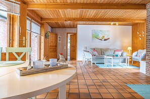 A cozy living room with a round table, a sofa, and a coffee table. There is a window with blinds, a door, and a brick wall. - Natur&Strand Vacation Rental (Flensburg)