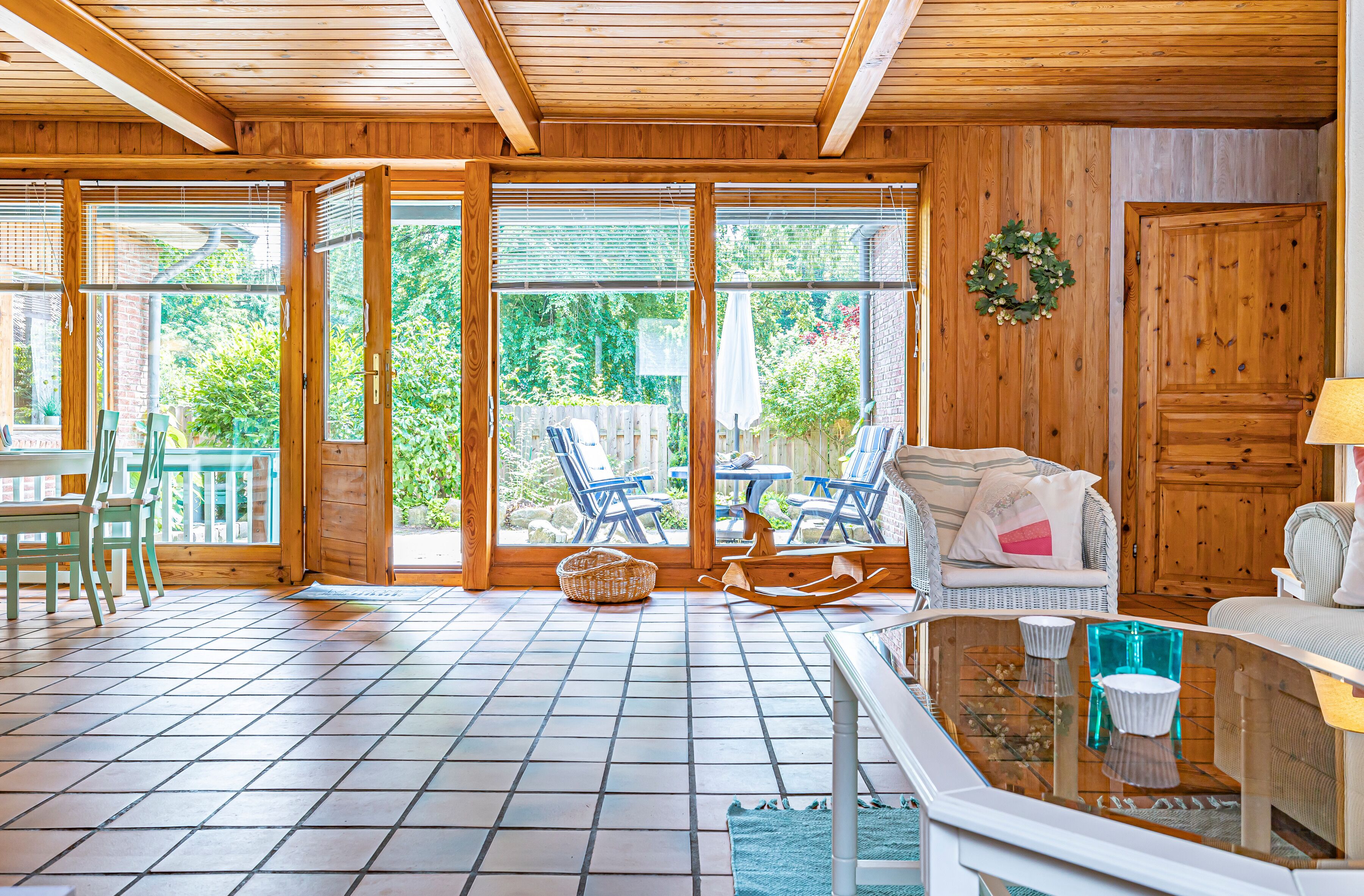 A wooden interior with a tiled floor, a wicker basket, a rocking chair, and a sofa with cushions.
