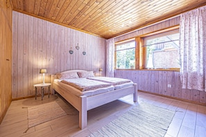 A bedroom with a wooden ceiling, a bed, a nightstand, a window with curtains, and a view of the outside. - Natur&Strand Vacation Rental (Flensburg)