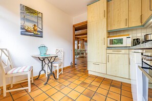 A kitchen with wooden cabinets, a tiled floor, a table with chairs, and a painting on the wall. - Natur&Strand Vacation Rental (Flensburg)