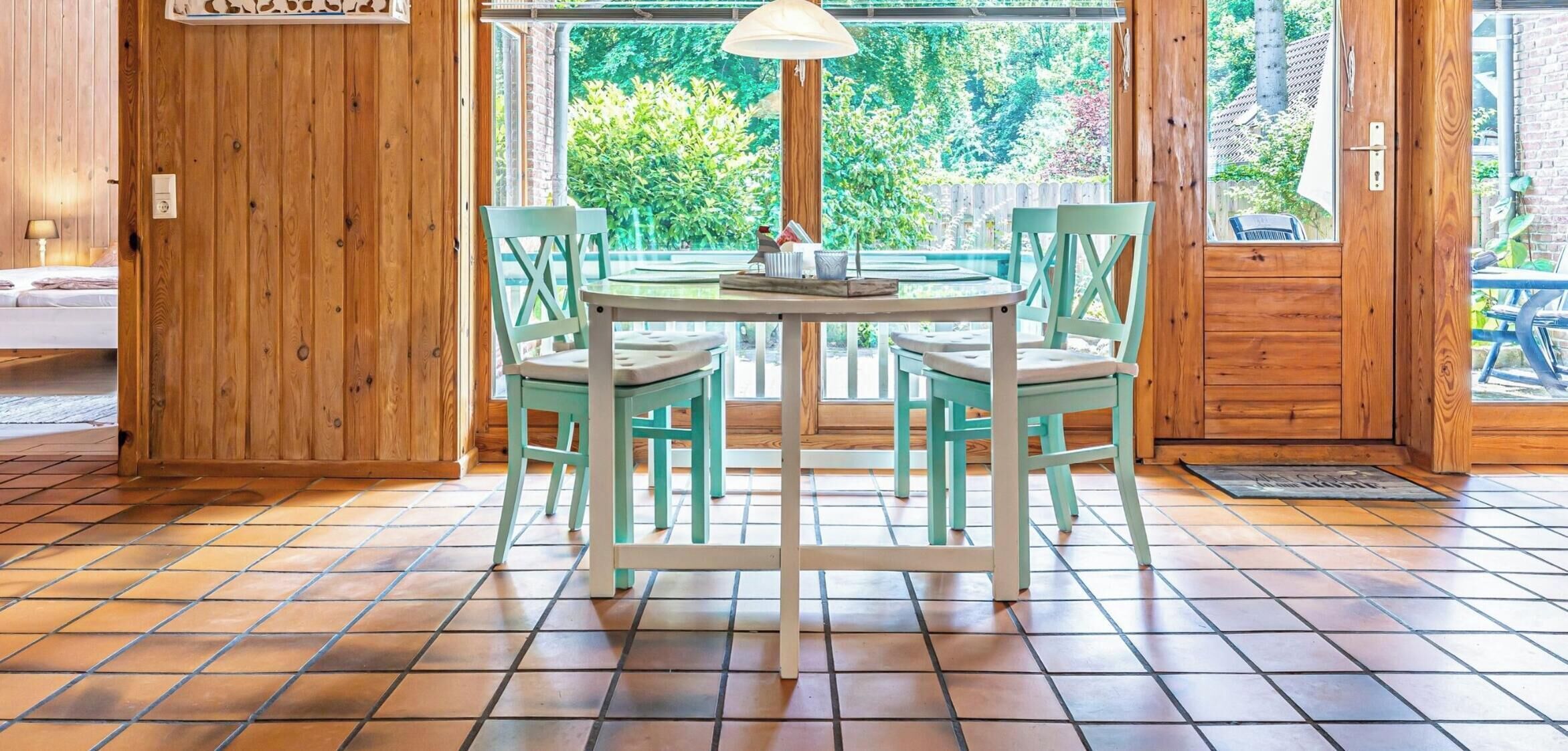Ein Holzinterieur mit einem runden Tisch, vier Stühlen, einer Lampe und Blick ins Grüne.
