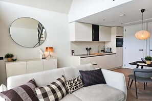 A modern living room with a sofa, a round mirror, and a dining area with a table and chairs. - Holiday apartment with 1 bedroom (Domburg)