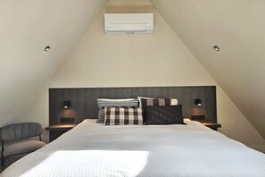 A modern bedroom with a sloped ceiling, a large bed with multiple pillows, bedside lamps, and an air conditioning unit. - Holiday apartment with 1 bedroom (Domburg)