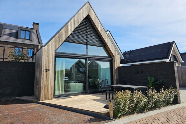 A modern house with a sloped roof, large glass windows, and a patio area with outdoor furniture. - Holiday apartment with 1 bedroom (Domburg)