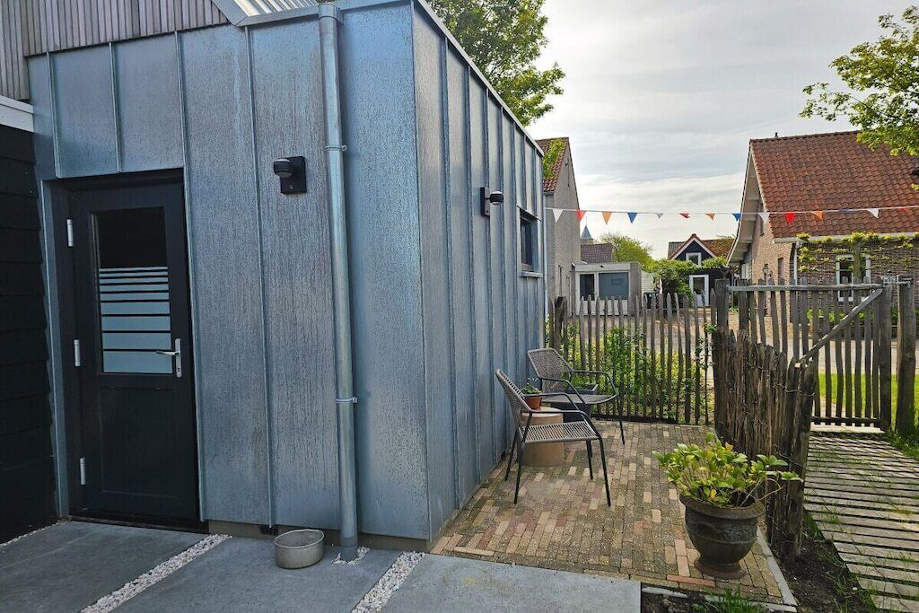 Eine Metallhütte mit Tür, eine kleine Außenbereich-Sitzgelegenheit mit Stühlen und Tisch, sowie ein eingezäunter Garten.