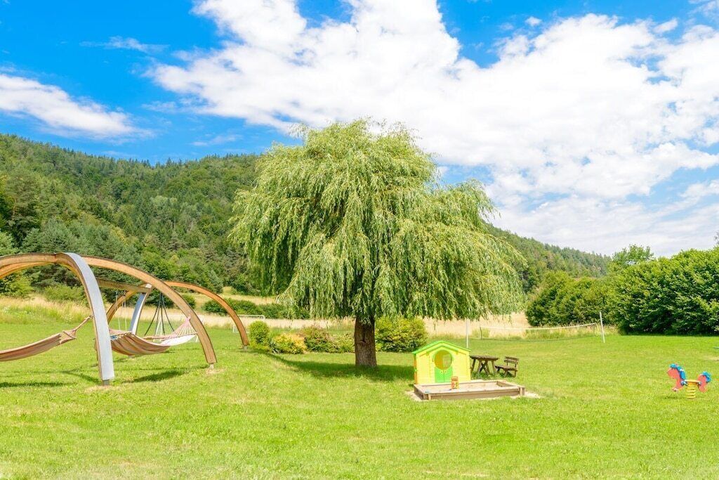 Un espace extérieur verdoyant avec une balançoire, un petit arbre et une cabane de jeu.