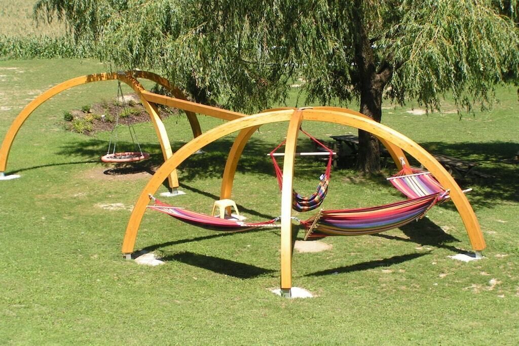 A hammock swing structure in a grassy area with trees in the background.