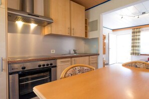 Eine Küche mit Holzschränken, einer Edelstahl-Dunstabzugshaube, einem eingebauten Backofen und einem Esstisch mit Stühlen.