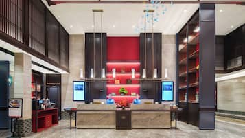A hotel reception area with a marble floor, a reception desk, and a red accent wall.