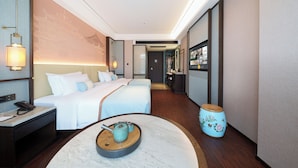 A hotel room with a bed, bedside table, lamp, and a small table with a teapot.