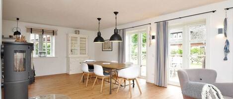 A spacious living area with a wooden floor, a dining table with chairs, a sofa, and a fireplace.