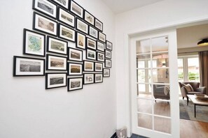 A room with a wall of framed photographs, a sliding glass door leading to an outdoor area with seating. - Holiday home with 1 bedroom (St.Peter-Ording)