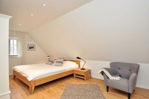 A bedroom with a wooden bed, a nightstand, a chair, and a window. - Holiday home with 1 bedroom (St.Peter-Ording)