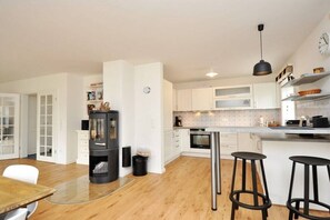 A modern kitchen with white cabinets, a black stove, and a glass-top dining table with bar stools. - Holiday home with 1 bedroom (St.Peter-Ording)