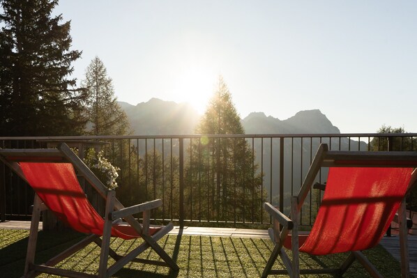 Deux chaises pliantes rouges sur un balcon, avec vue sur les montagnes et les arbres.