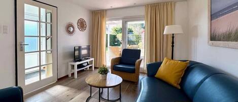 A living room with a blue sofa, a television, a small round table with a plant, and a chair.