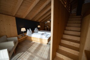 Una escalera de madera que lleva a un dormitorio con una cama, lámparas de noche y una silla.