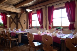 Un restaurante con mesas y sillas de madera, cortinas rojas y lámparas colgantes.