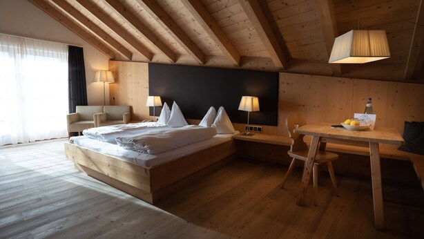 Un dormitorio con piso de madera, una cama, lámparas de noche, un escritorio y una silla.