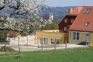 Ein gelbes Gebäude mit einer Steinmauer, ein Haus mit rotem Dach und eine Kirche im Hintergrund.