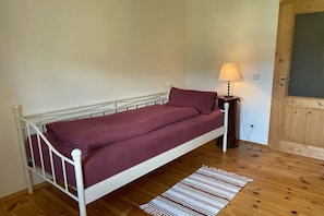 Ein Einzelbett mit weißem Gestell und einer roten Matratze in einem Zimmer mit Holzboden.