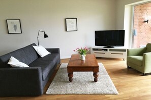 A living room with a dark sofa, a wooden coffee table, a flat-screen TV, and a green armchair. - Marina-Fördeblick (Luck 2) (Glücksburg)