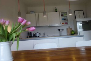 Une cuisine moderne avec des meubles blancs, un plan de travail en bois et un coin repas agrémenté d’un vase de tulipes roses.