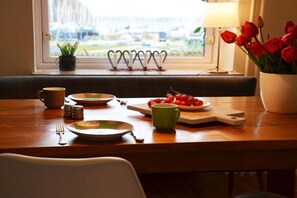 A dining table set with plates, cups, and a bowl of cherries, with a window view in the background. - Marina-Fördeblick (Luck 2) (Glücksburg)