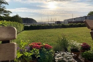 Un espace extérieur verdoyant, agrémenté de plantes en pot, d’où l’on peut admirer des voiliers au loin.