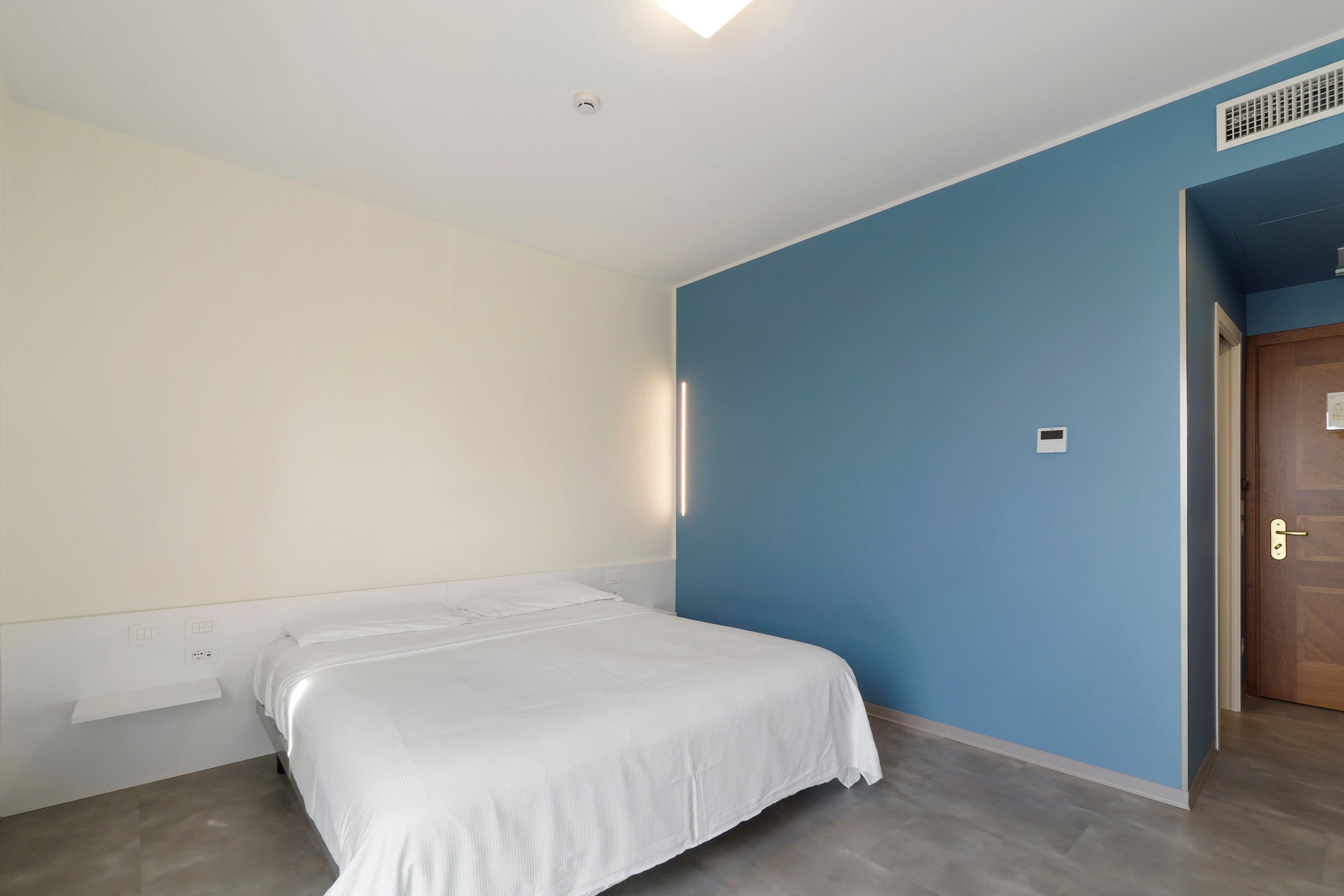 Ein Schlafzimmer mit einem Einzelbett, einer blauen Akzentwand und einer Holztür.