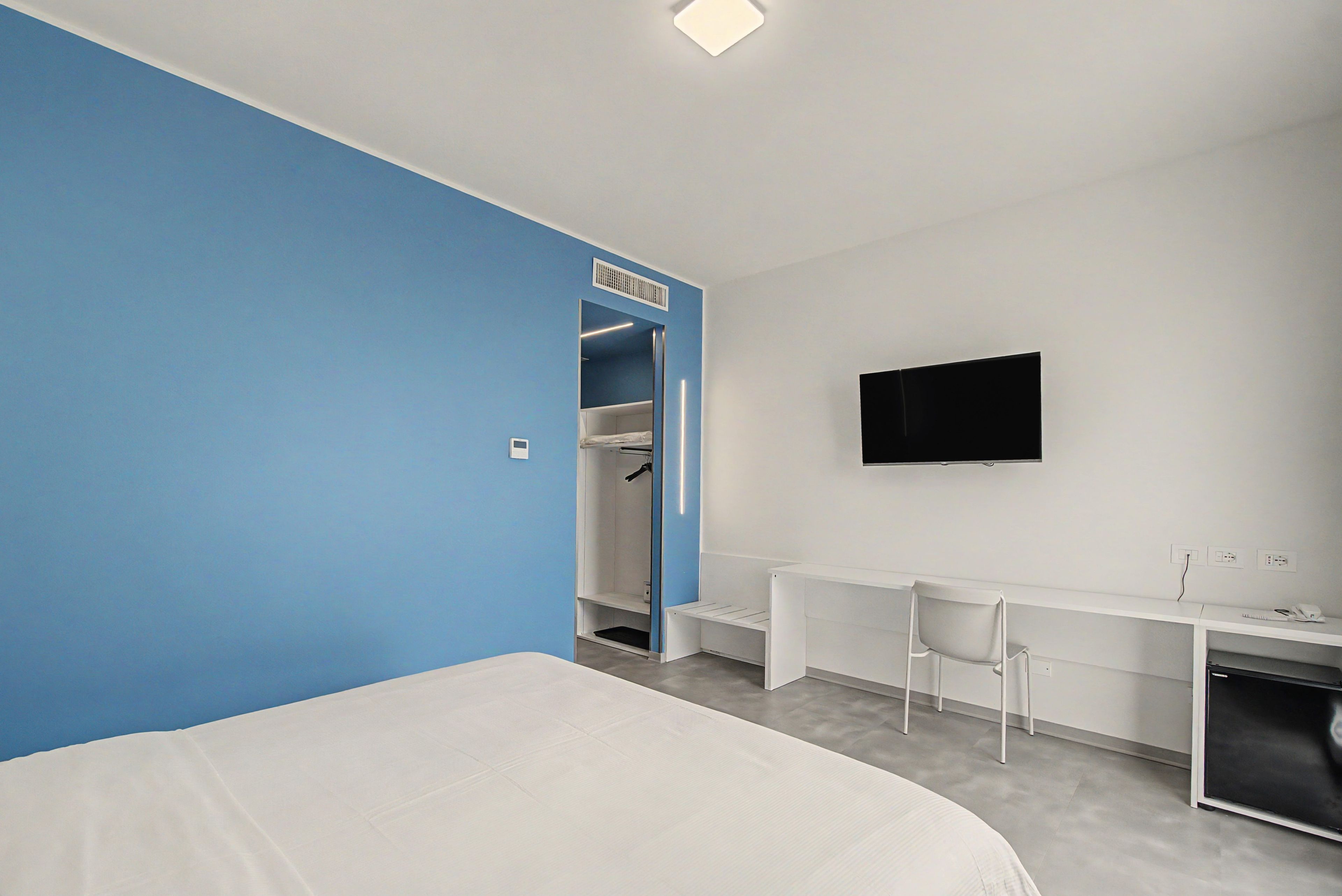Ein Hotelzimmer mit Bett, Schreibtisch, Fernseher und begehbarem Kleiderschrank.