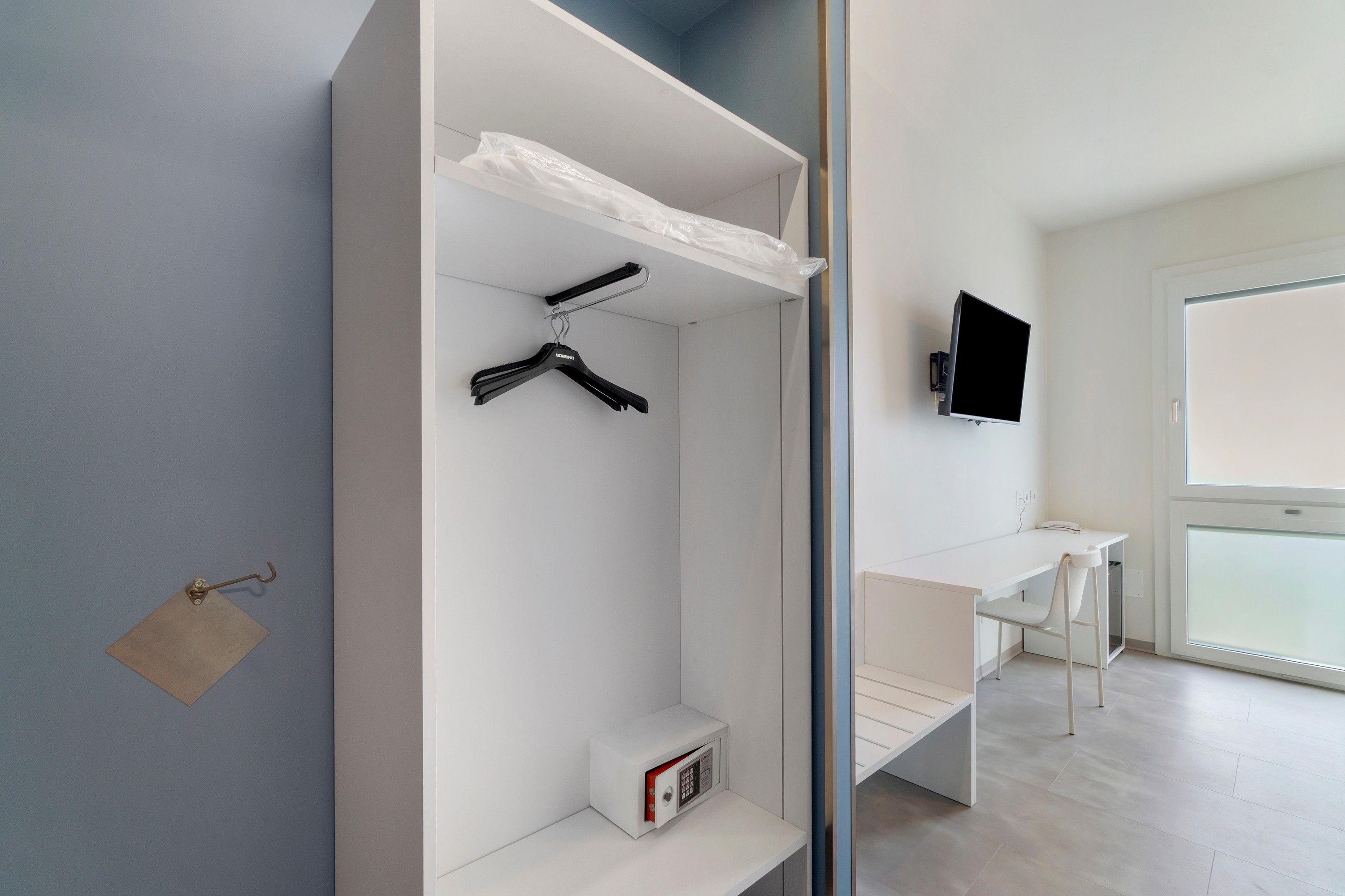 Une chambre moderne avec une armoire blanche, un bureau et un téléviseur.