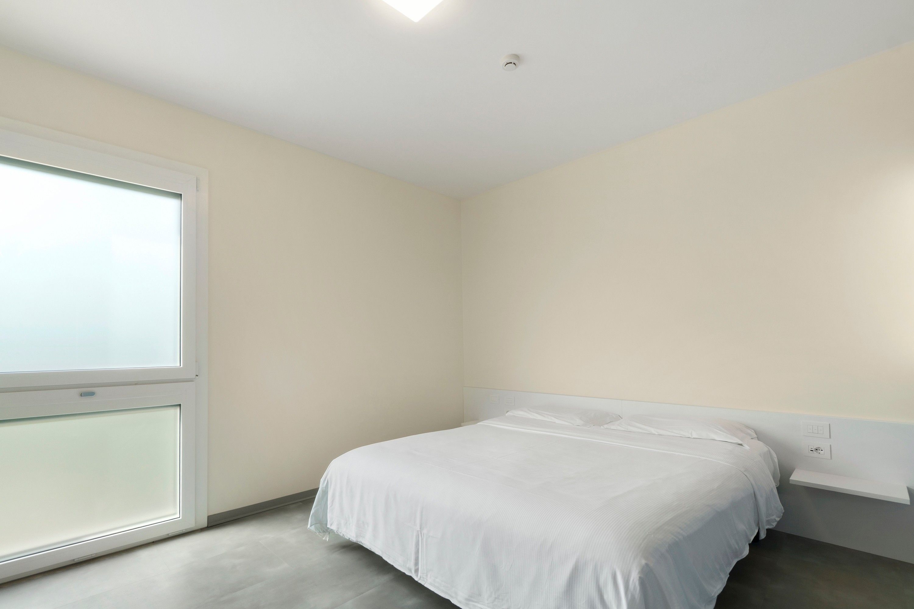 Ein Schlafzimmer mit einem Einzelbett, einem Fenster und einer weißen Decke.
