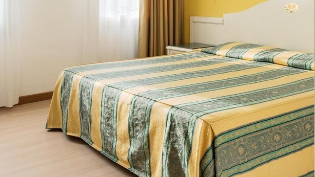 Una camera d'albergo con un letto, tende, un comodino e una lampada a muro.