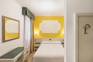 Een hotelkamer met een bed, nachtkastje, lamp en een deur.