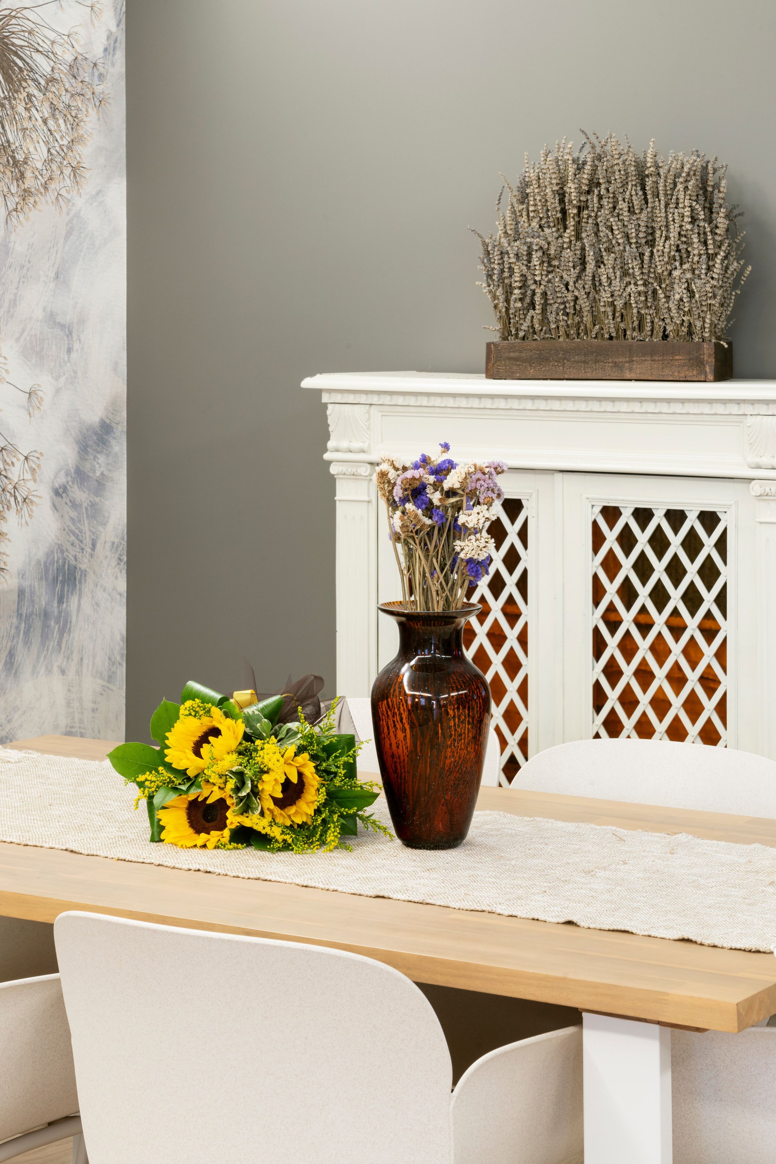 A dining table with a vase of sunflowers and a decorative arrangement on a mantelpiece.