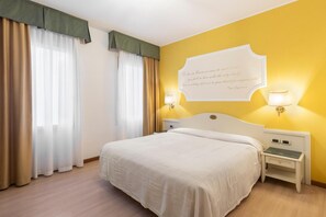 Een hotelkamer met een bed, twee nachtkastjes met lampen, een muisbrief en gordijnen.